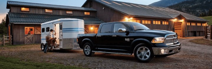 Black pickup truck with a horse trailer parked by a barn, mountains in the background.
