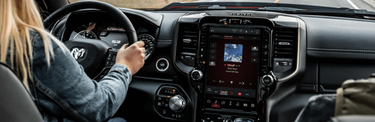 Person driving a RAM vehicle with focus on the dashboard and infotainment system display.