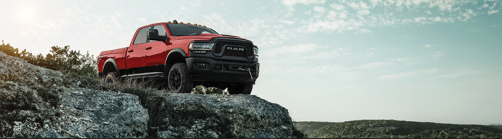 Red pickup truck on rocky terrain under a blue sky, showcasing off-road capability and ruggedness.