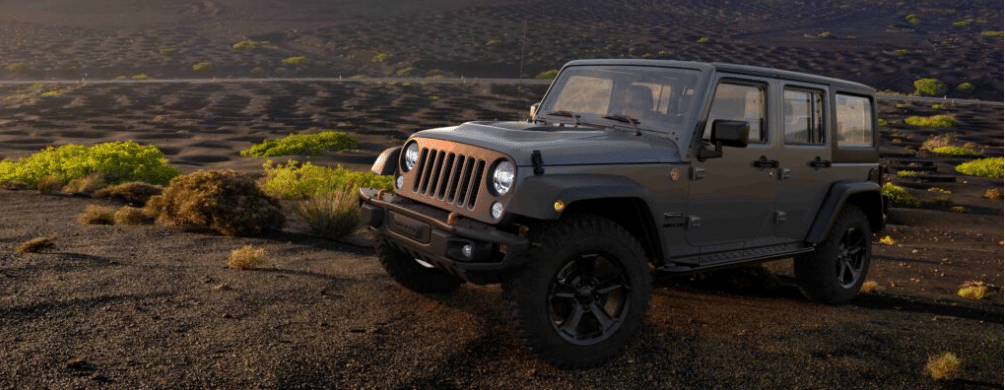 A rugged off-road SUV parked on a rocky terrain with sparse greenery under a setting sun.