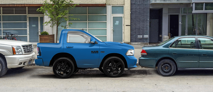 Blue compact pickup truck parked tightly between two larger cars on a city street.