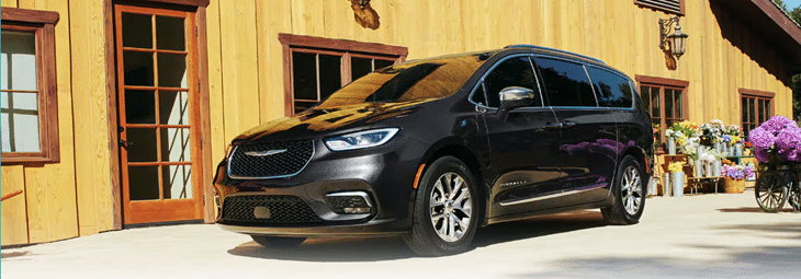 A sleek black minivan parked by a rustic wooden building with potted flowers nearby.