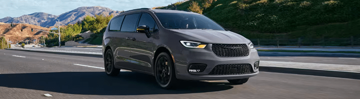 Gray minivan driving on a highway with scenic mountains in the background.