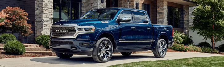 Blue Ram pickup truck parked in front of a modern house with stone facade and landscaped garden.