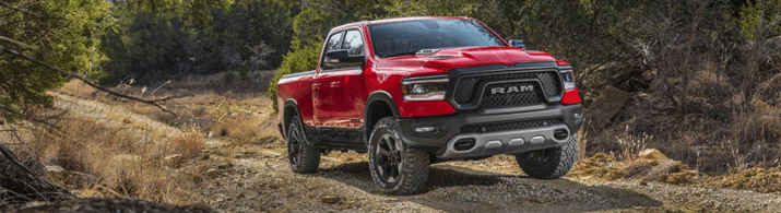 Red Ram pickup truck driving on a rugged dirt road surrounded by trees and dry grass.