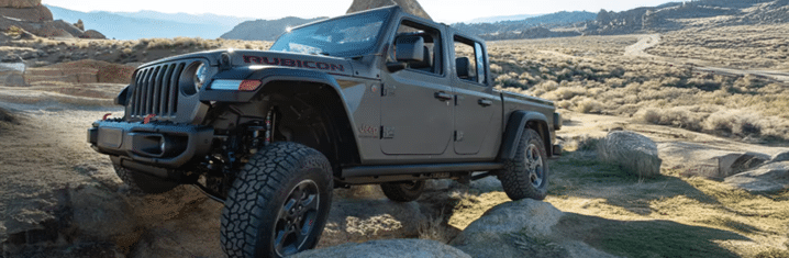 Jeep Rubicon pickup truck navigating rocky terrain with mountains in the background.