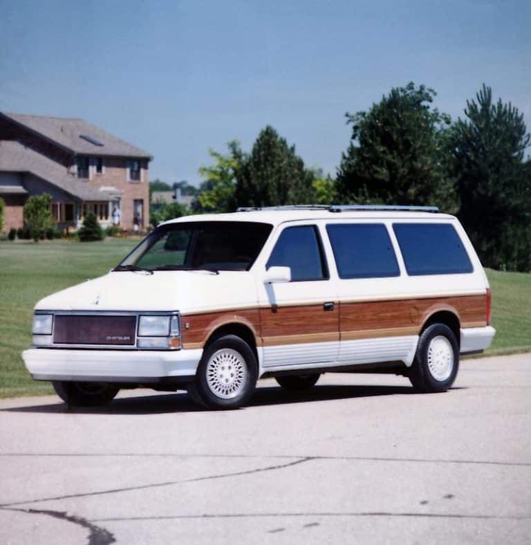 Vintage minivan with wood paneling parked in a suburban neighborhood with trees and houses.