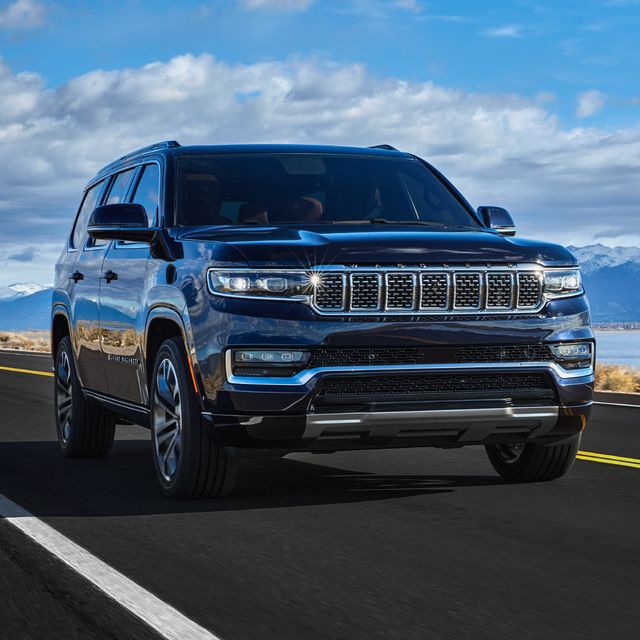 Black SUV driving on a scenic road with mountains and a blue sky in the background.