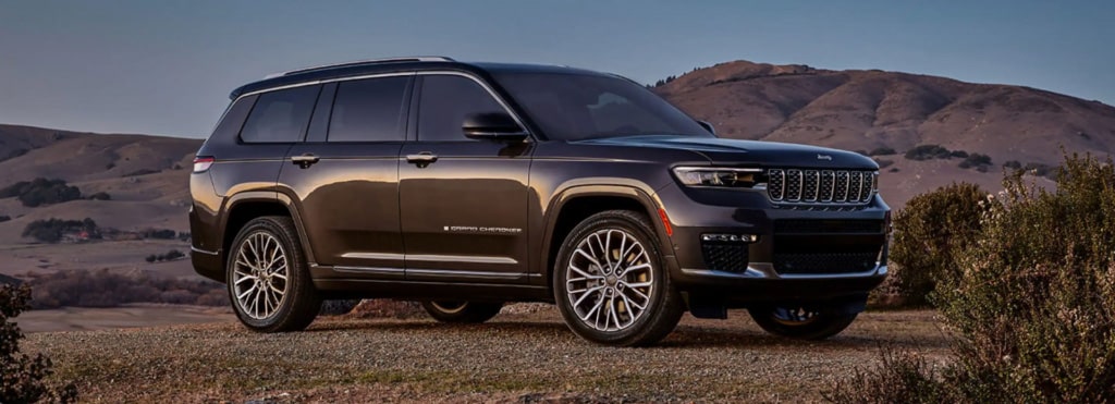 A dark SUV parked on a scenic hilltop at sunset, with rolling hills in the background.