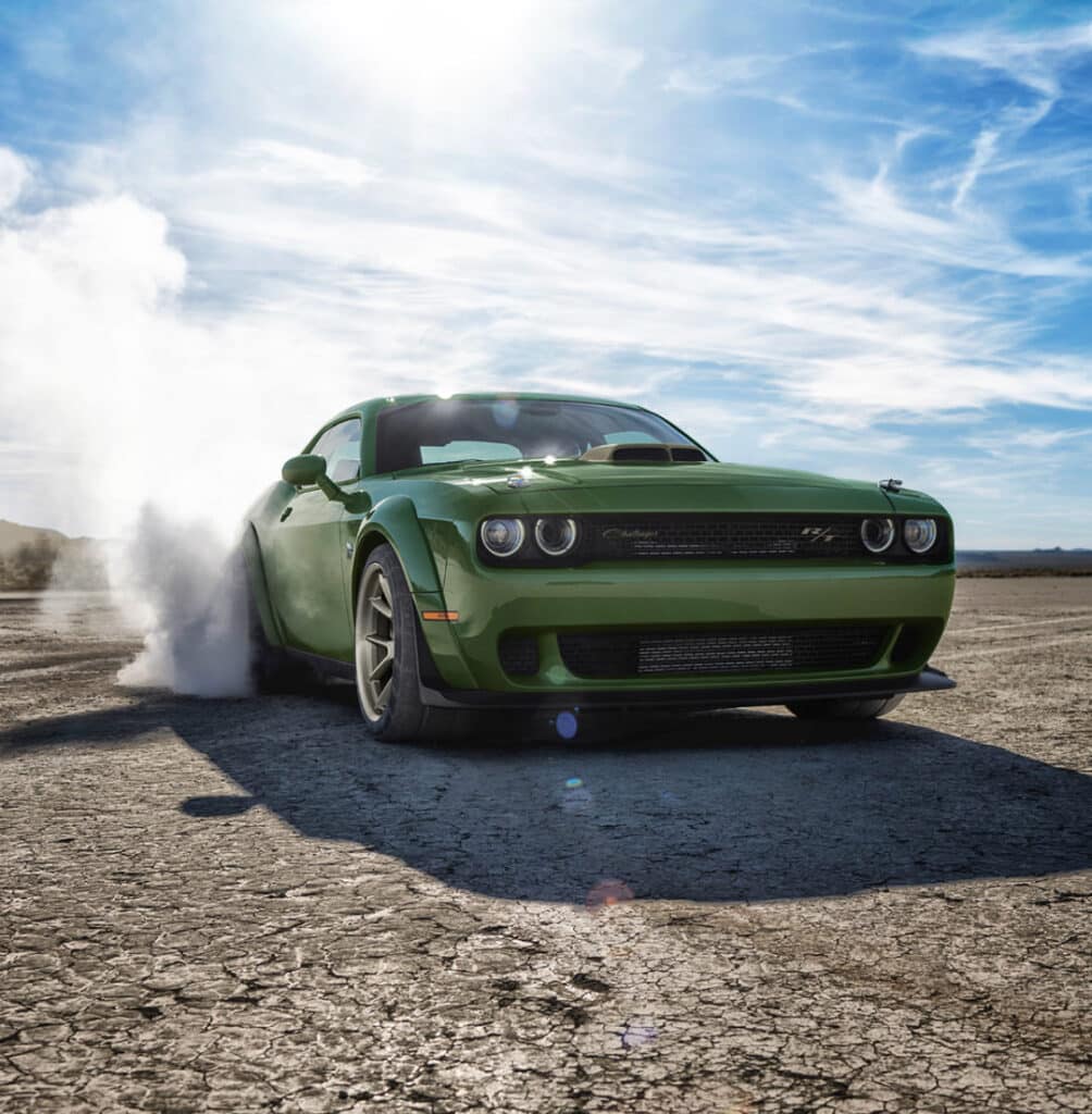 Green sports car performing a burnout on a dry, cracked landscape under a bright blue sky.