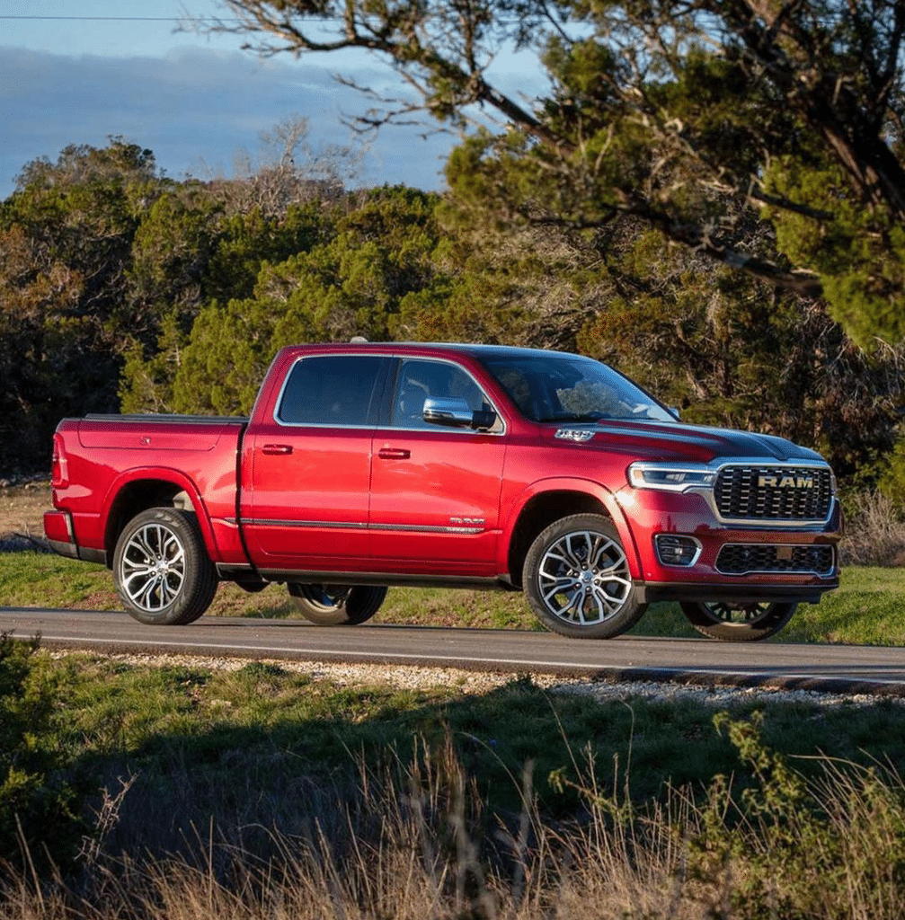 Red pickup truck parked on a road, surrounded by trees and grassy landscape under a clear blue sky.
