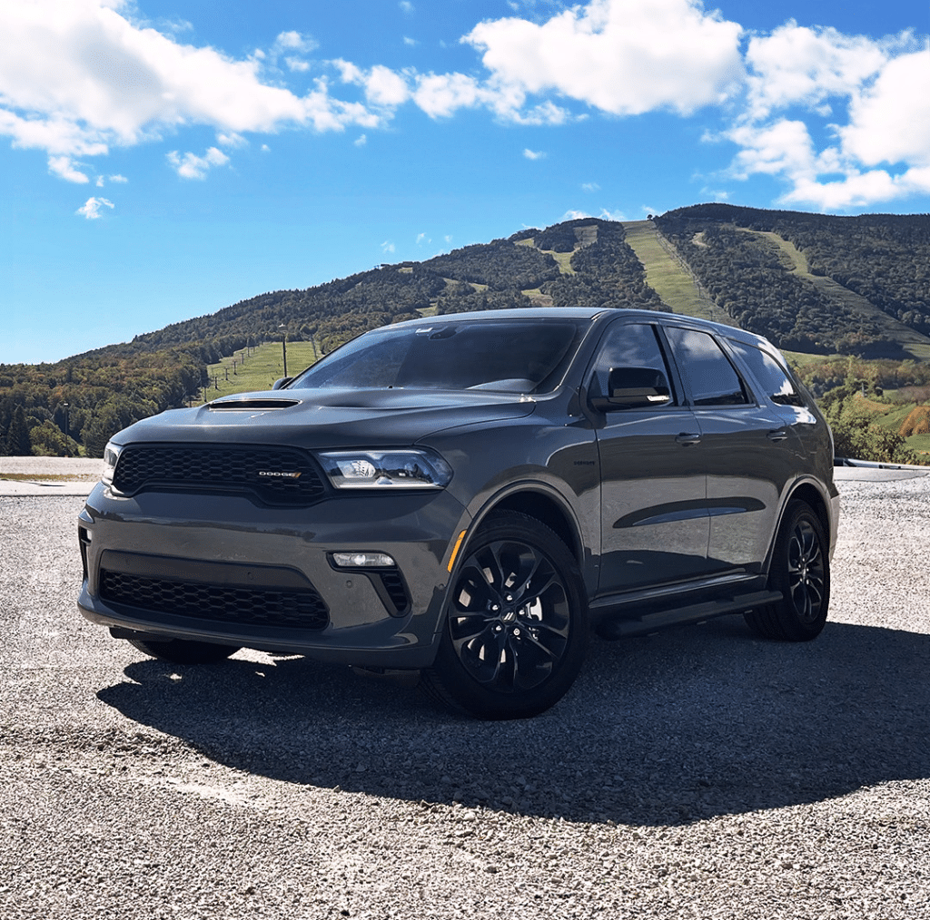 Gray SUV parked on a scenic mountain landscape under a clear blue sky with white clouds.