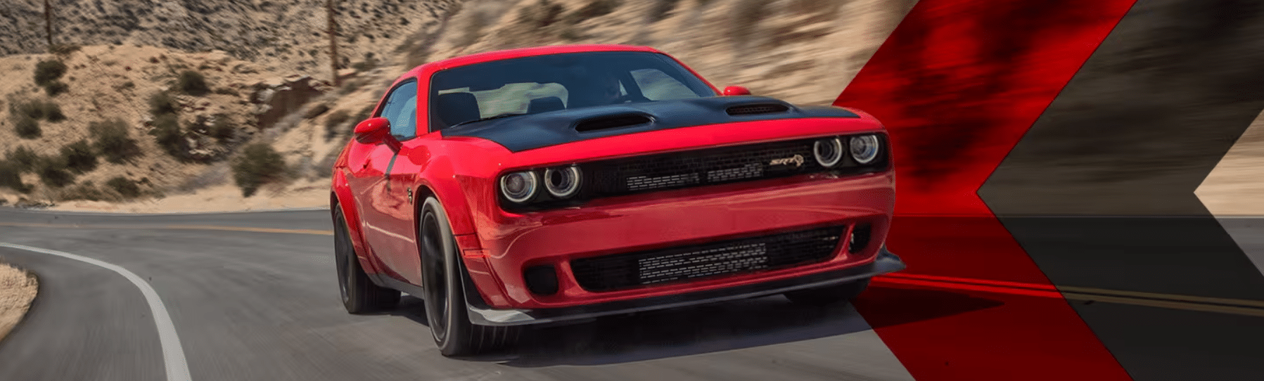 Red sports car with black hood driving on a desert highway curve, showcasing speed and design.
