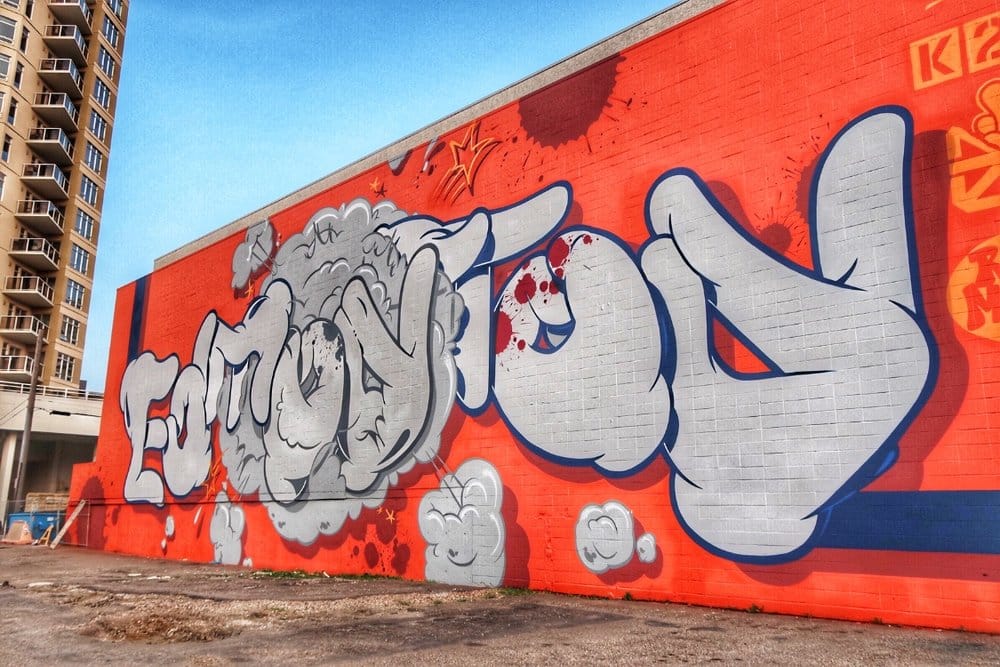 Graffiti mural on a red brick wall with bold, stylized letters and cloud-like designs.
