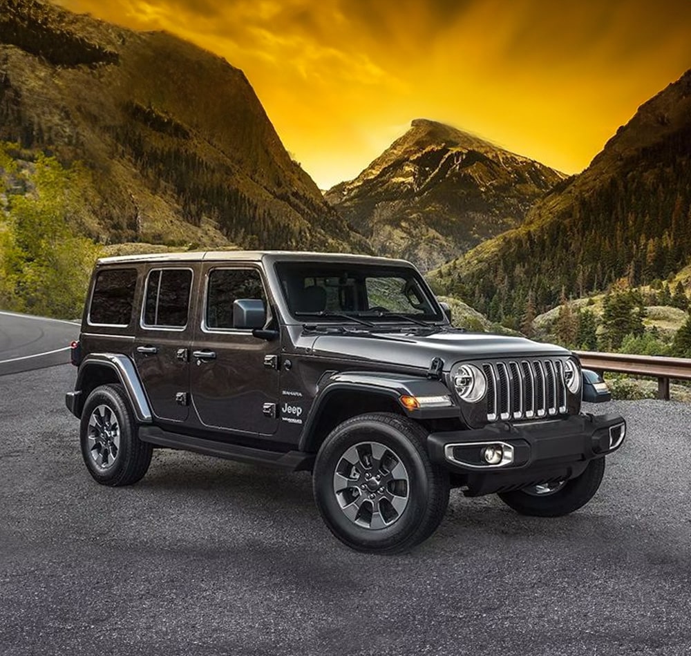 Black Jeep Wrangler on a mountain road at sunset, with dramatic skies and rugged terrain backdrop.