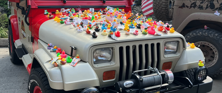 Jeep covered with colorful rubber ducks on the hood, parked outdoors.