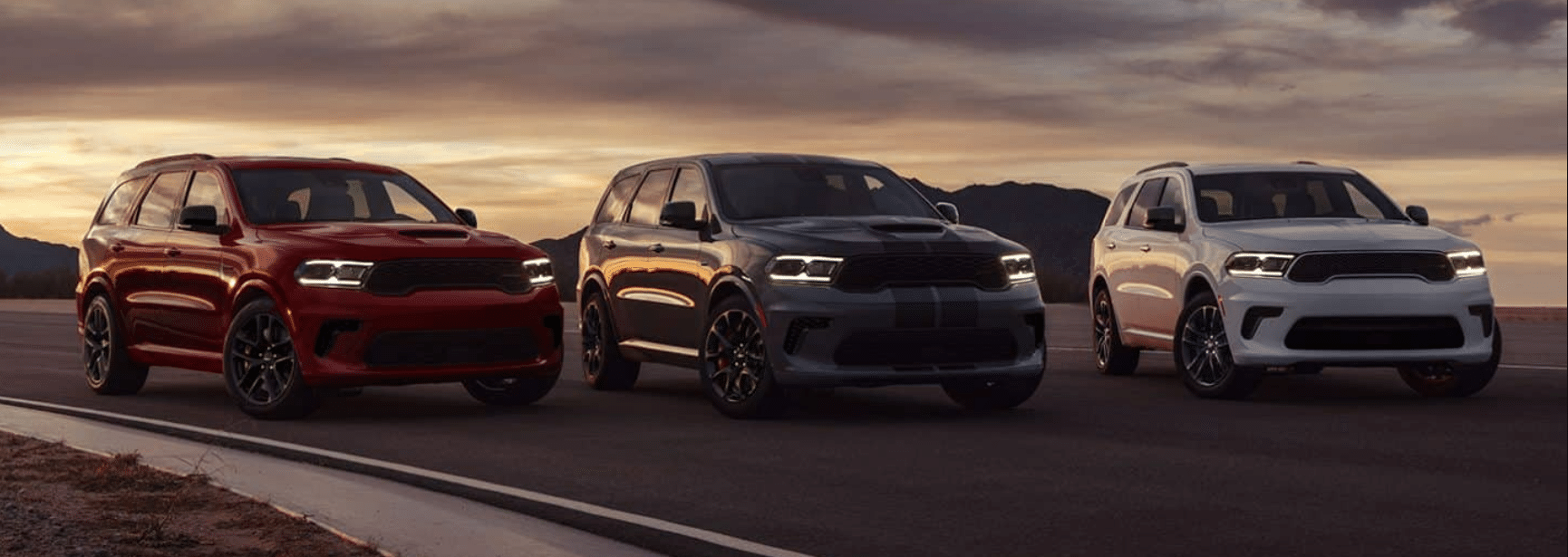 Three SUVs in red, blue, and white parked on a road during sunset in a mountainous setting.