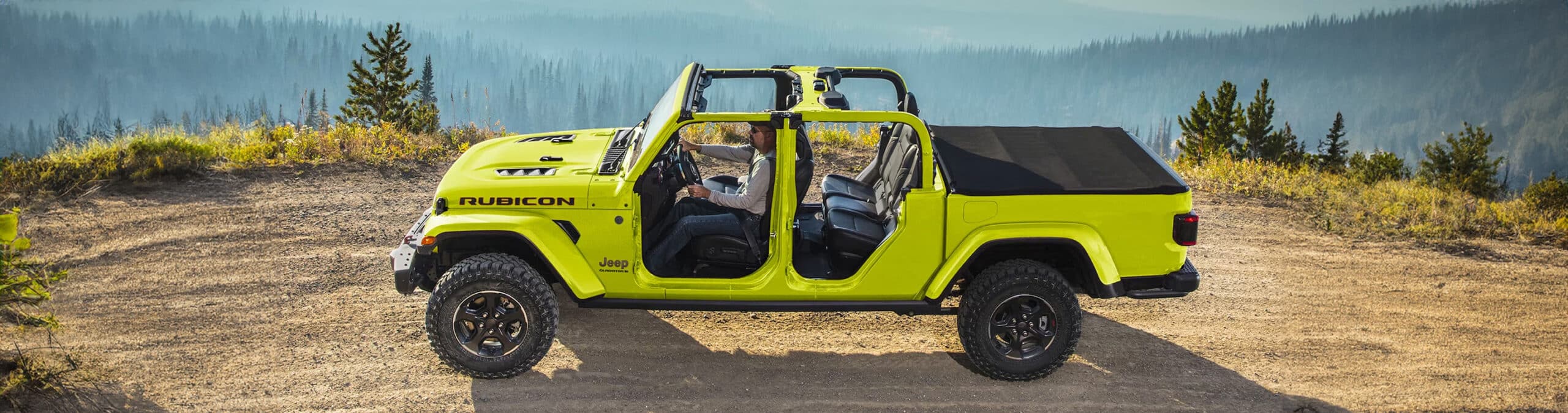 Bright yellow Jeep Rubicon parked on a dirt path with scenic mountain view in the background.
