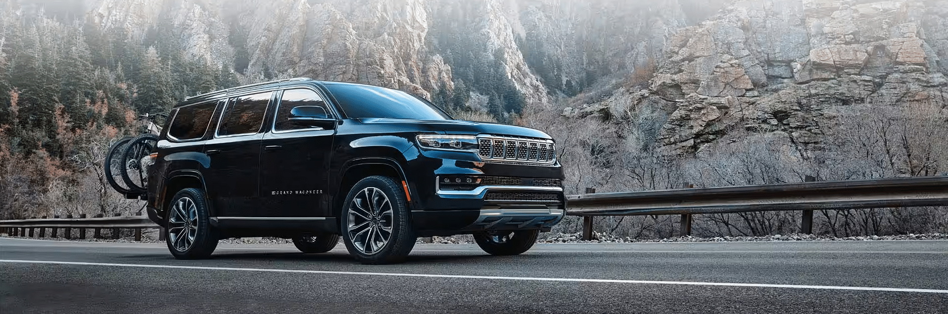 Black SUV with a bike rack driving on a scenic mountain road surrounded by rocky cliffs.