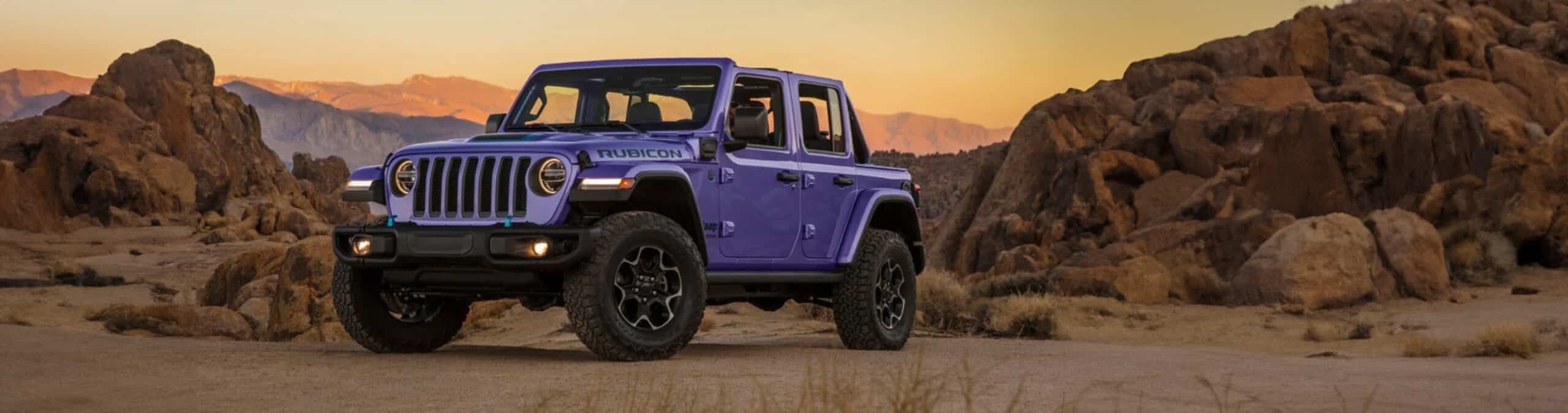 Purple Jeep Wrangler Rubicon parked on rocky desert terrain at sunset.