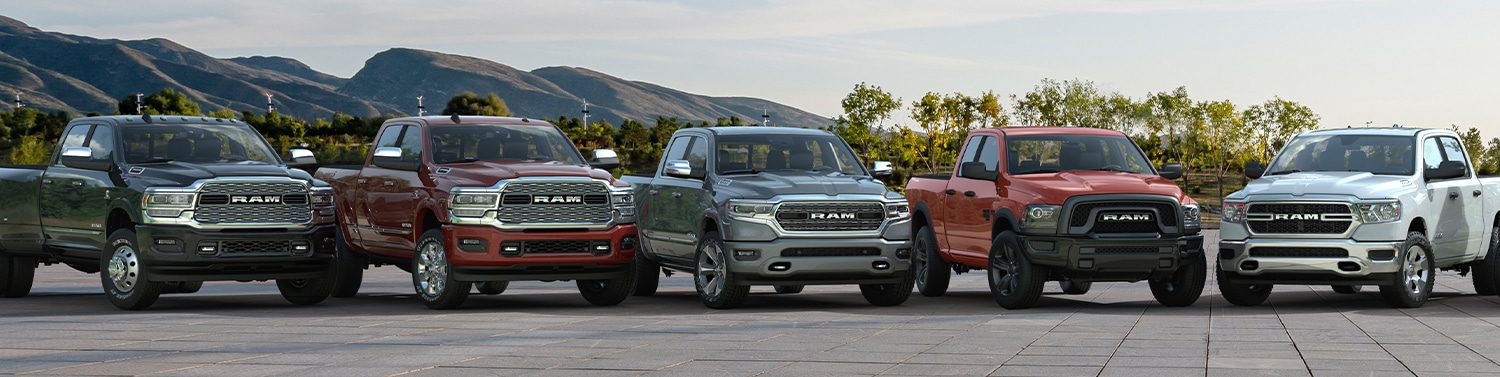 Lineup of RAM trucks parked outdoors, showcasing various models with mountains in the background.