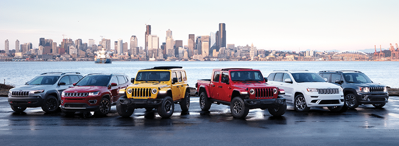 A lineup of colorful SUVs and trucks by a waterfront with a city skyline in the background.