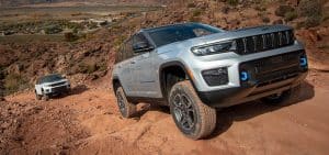 Two SUVs navigate a rocky off-road trail in a desert landscape under a clear sky.