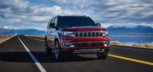 Red SUV driving on an open highway with mountains and clouds in the background.