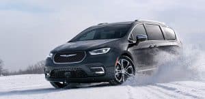 A gray minivan drives through snow, showcasing its winter handling capabilities on a snowy landscape.