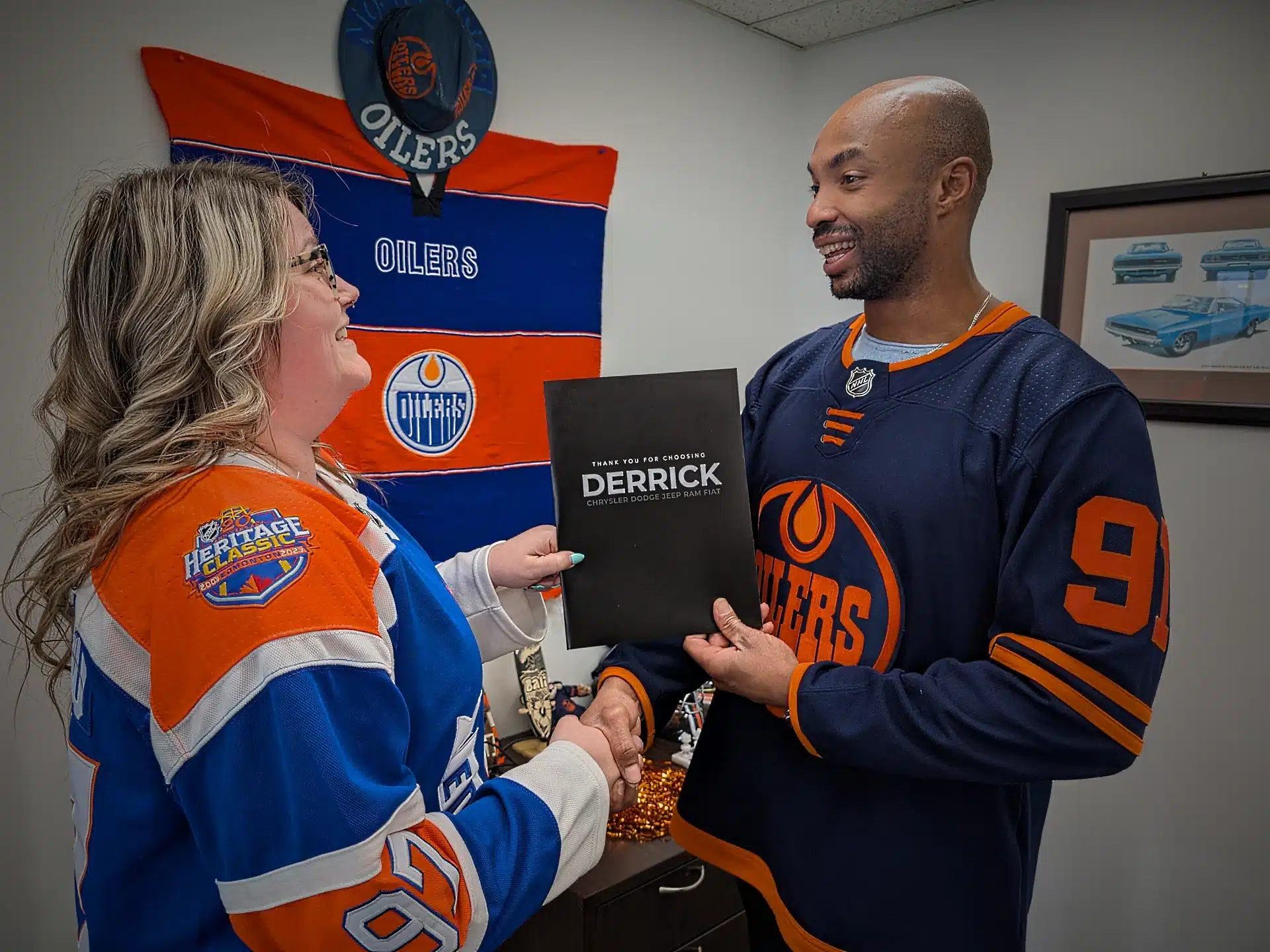 Two people in Oilers jerseys exchange a folder in an office with Oilers decor.