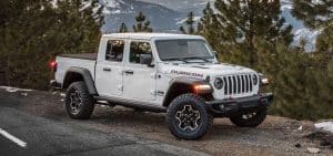 White Jeep Gladiator Rubicon parked on a mountainous road with pine trees in the background.