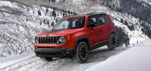 Red SUV driving on a snowy mountain road, showcasing winter capabilities and rugged design.