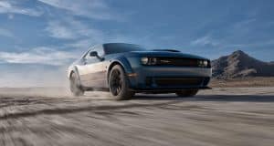 Blue sports car speeding on a desert road against a mountainous backdrop under a clear sky.