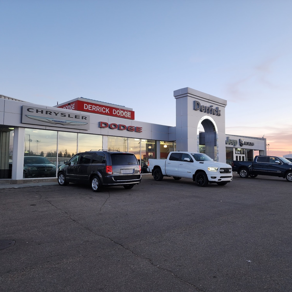 Car dealership at sunset featuring Chrysler, Dodge, and Jeep vehicles parked in front.