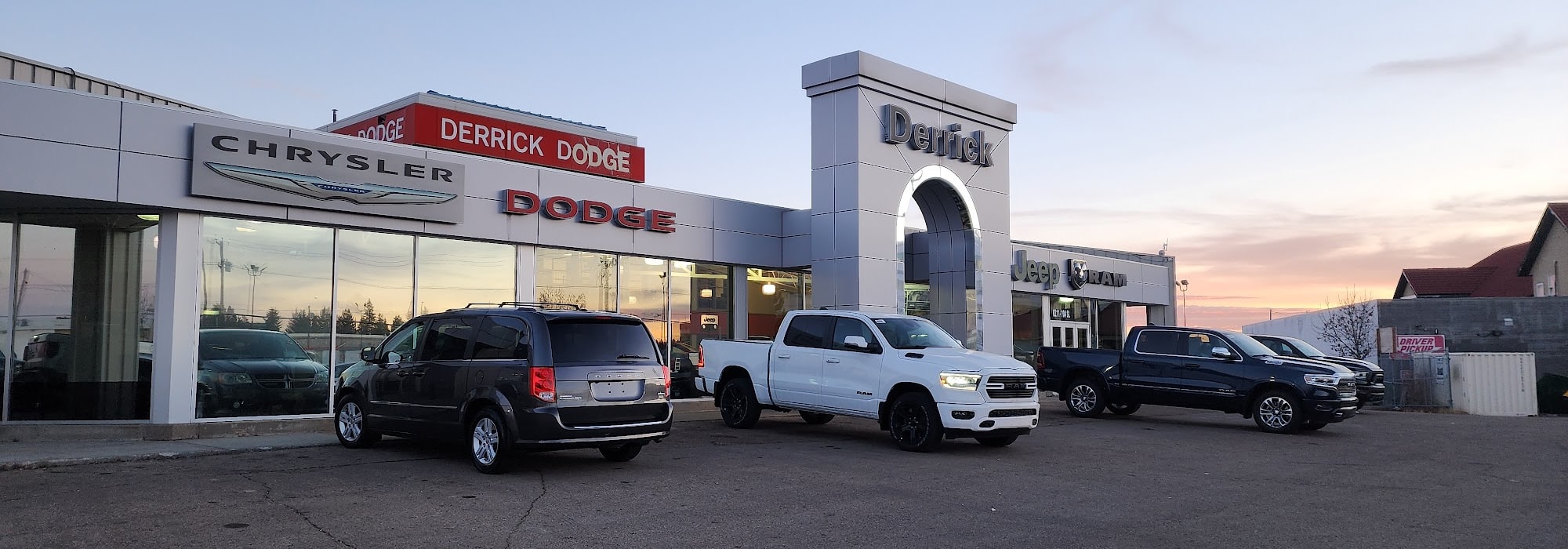 Car dealership exterior featuring Chrysler, Dodge, Jeep, and Ram vehicles at sunset.