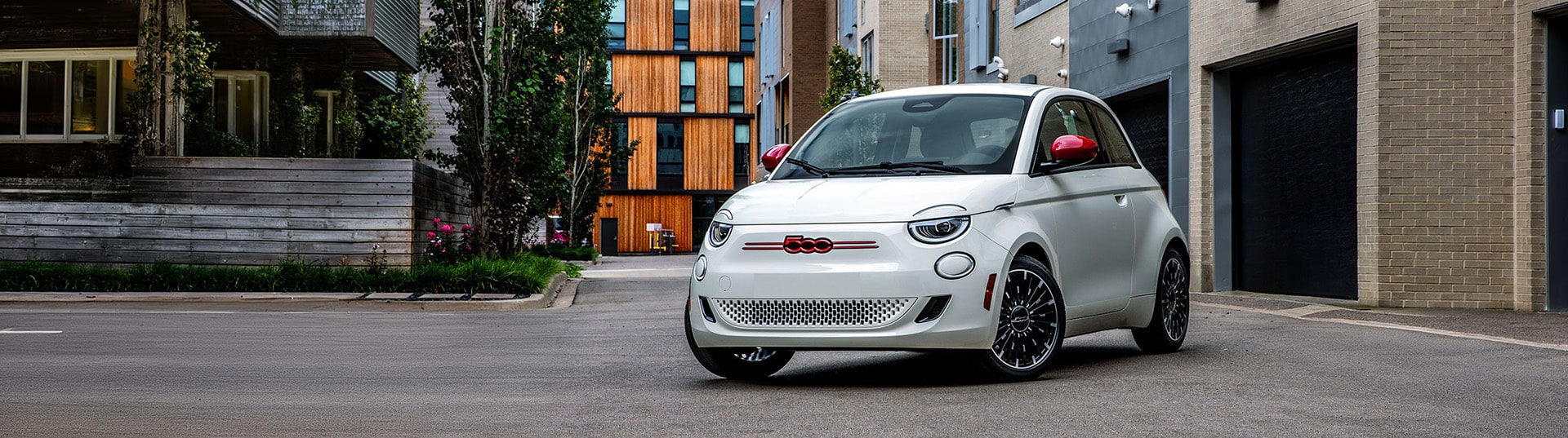 White compact car parked in an urban setting with modern buildings and greenery.