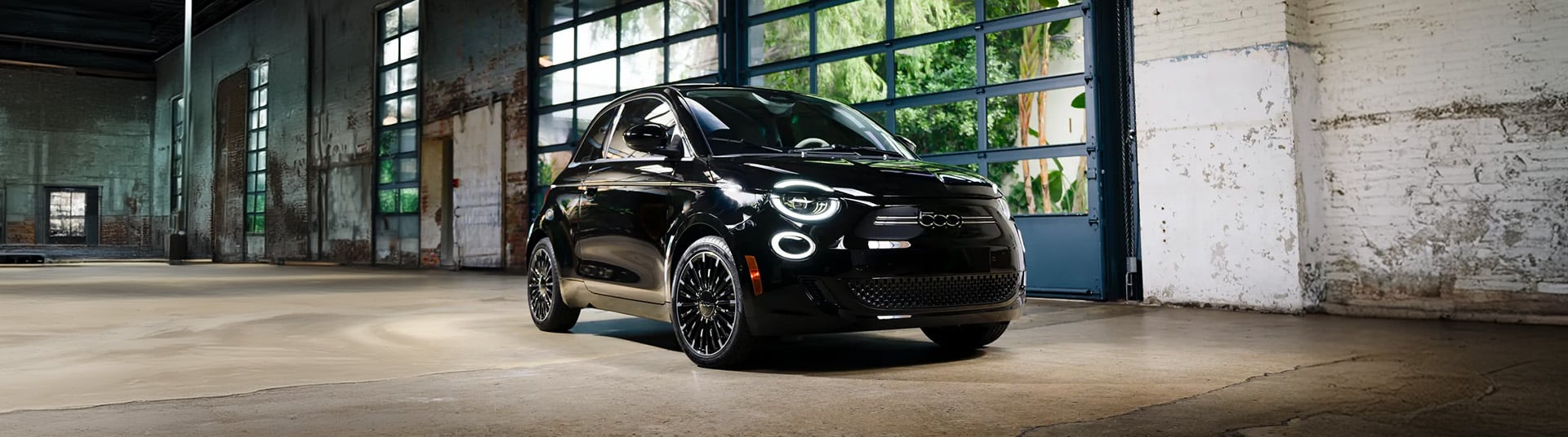 Black compact car in an industrial garage with large windows and textured walls.