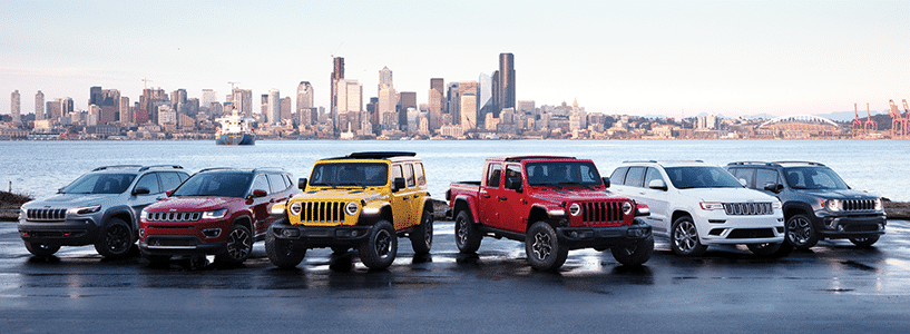 Six SUVs parked by a waterfront with a city skyline in the background at dusk.