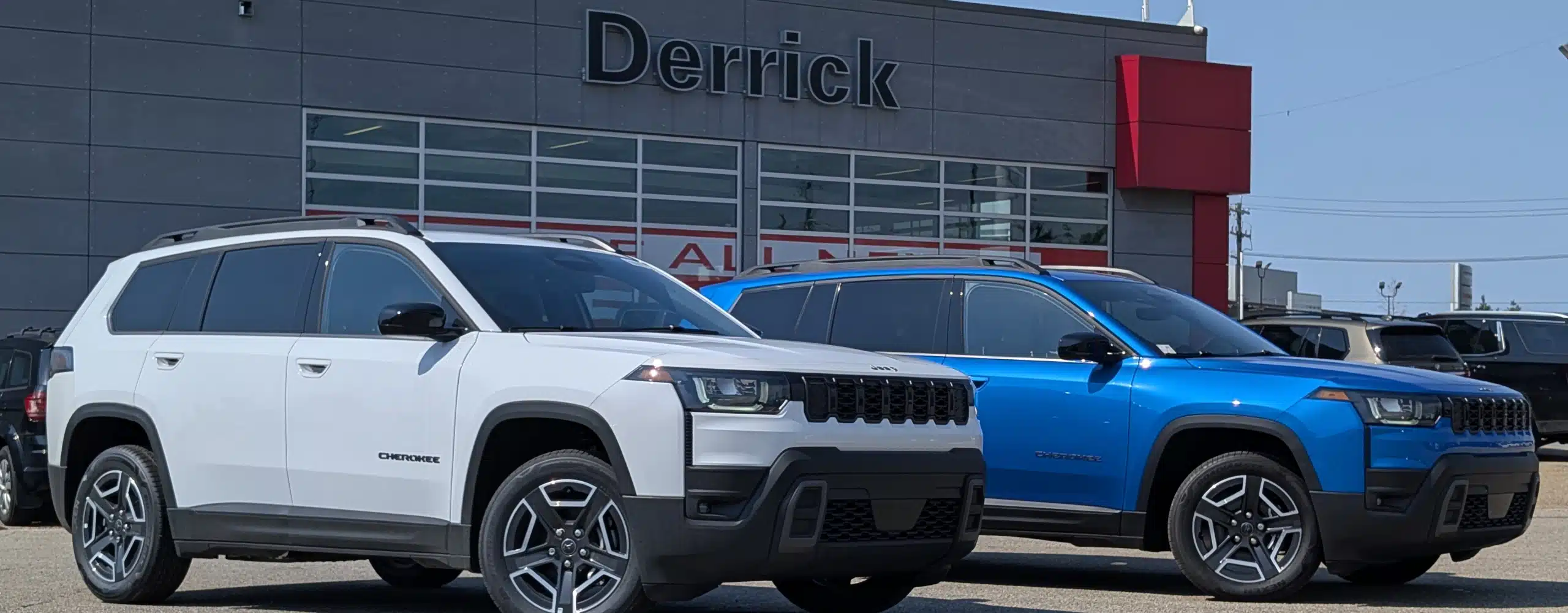 White and blue Cherokee SUVs parked outside a dealership with "Derrick" sign.